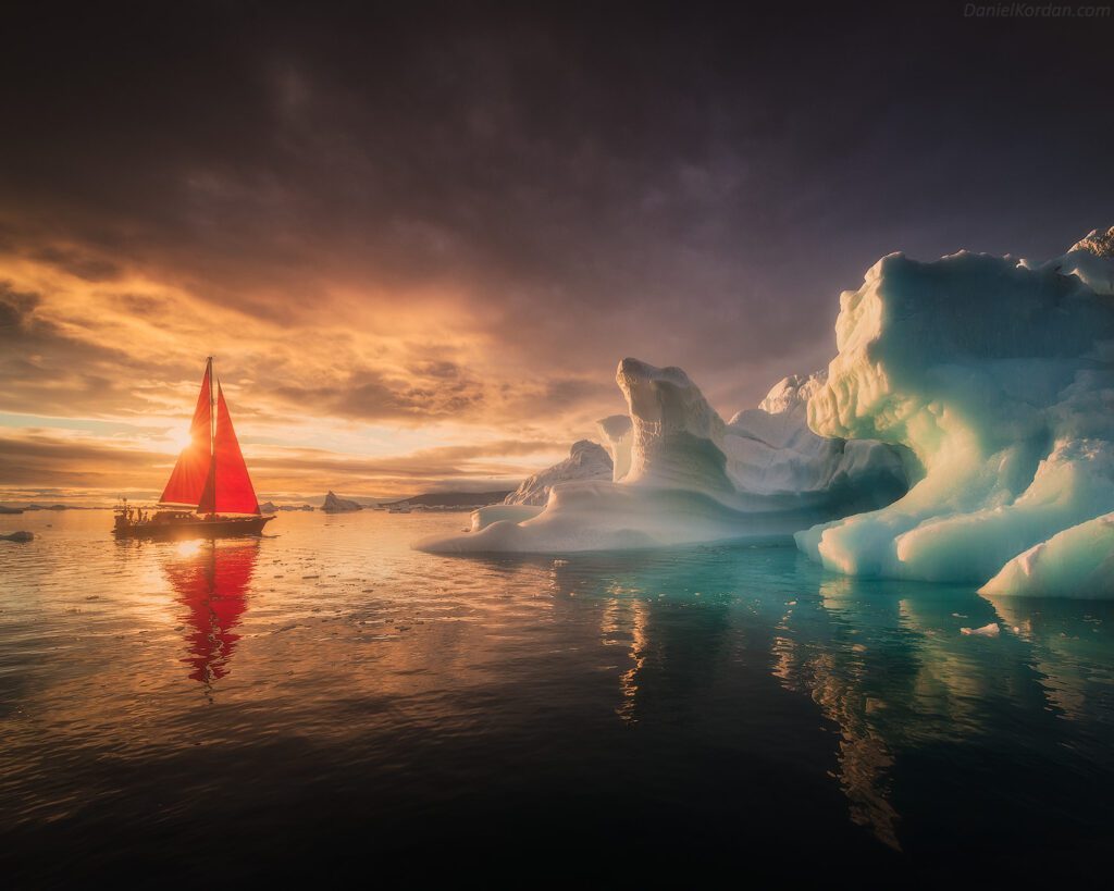 Red sailboat and giant iceberg at sunset in Greenland