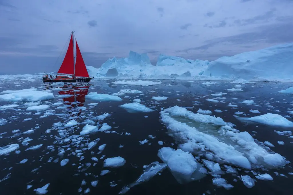 Red sailboat drifting amongst ice shards in Disko Bay, Greenland