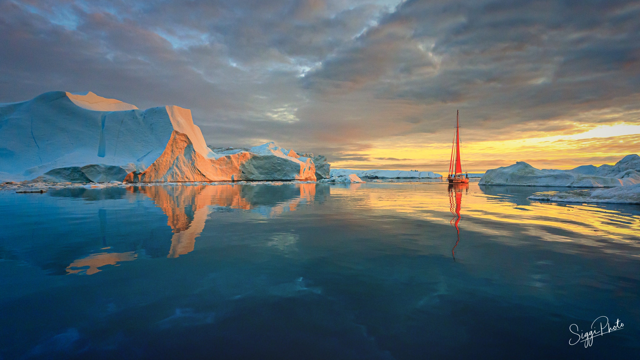 Red sailboat and icebergs at sunset in Greenland